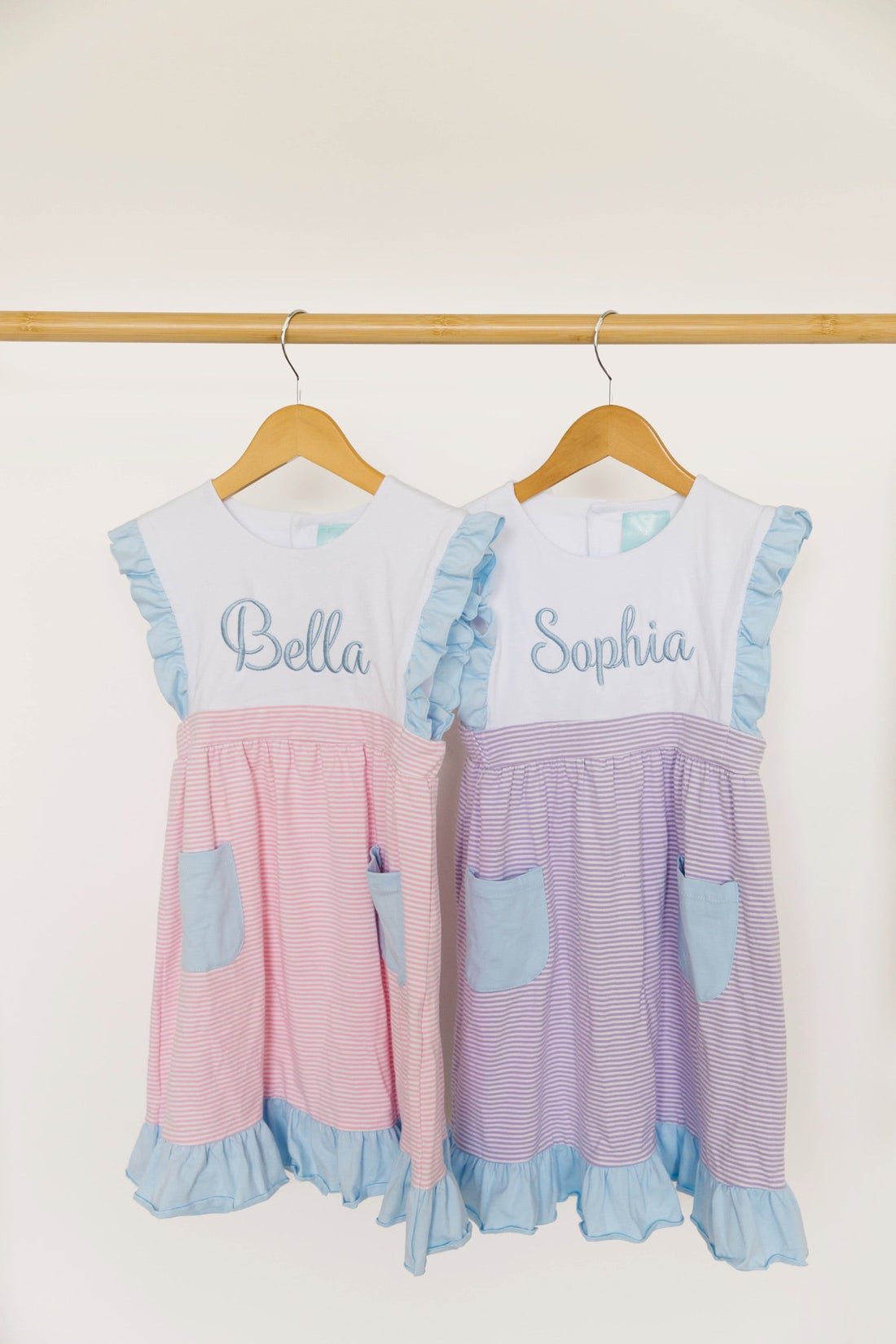 Personalized girls dresses with embroidered names hanging beside matching pastel backpacks