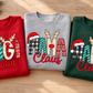 Folded red GiGi Claus, grey MAMA Claus and green NANA Claus adult Christmas sweatshirts on a wooden table.