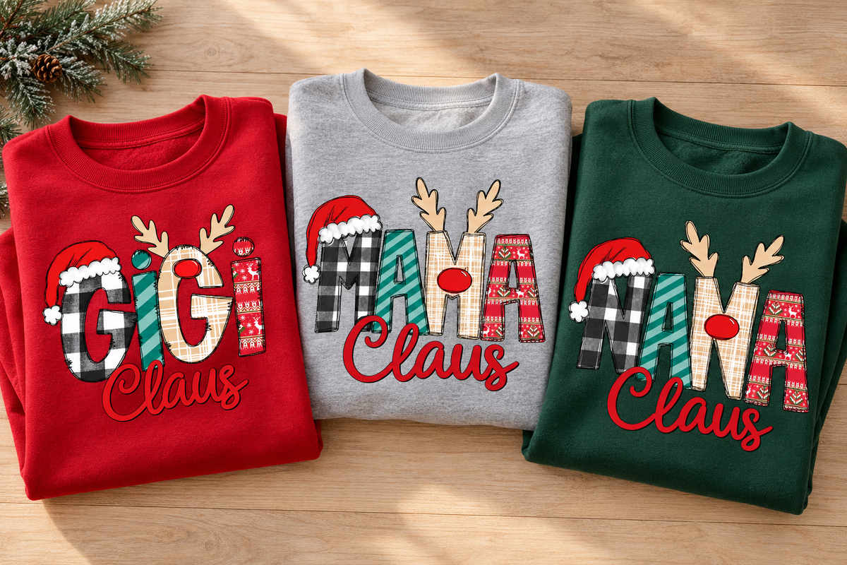 Folded red GiGi Claus, grey MAMA Claus and green NANA Claus adult Christmas sweatshirts on a wooden table.
