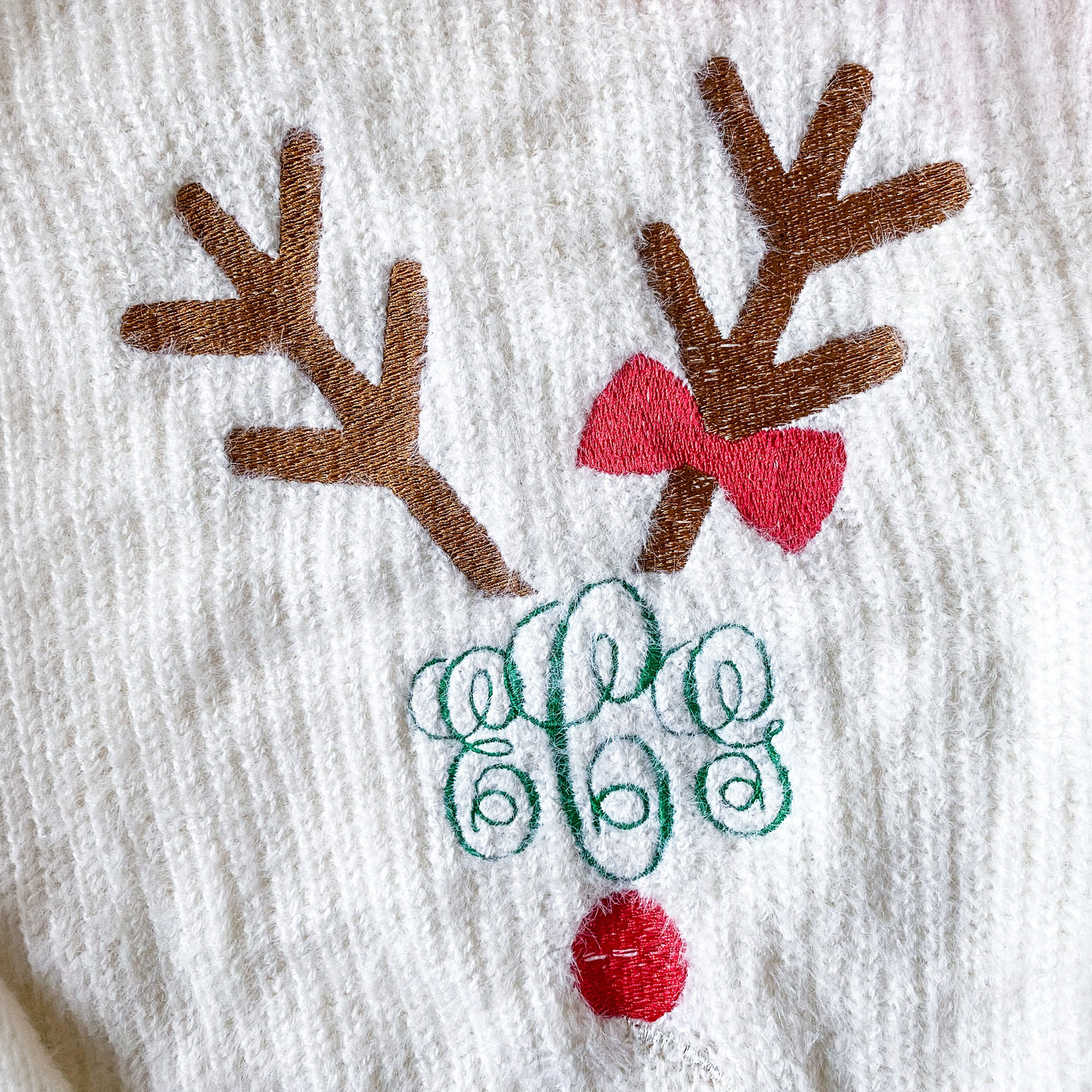 Close-up of embroidered reindeer design with antlers, red bow, monogram, and red pom-pom nose.
