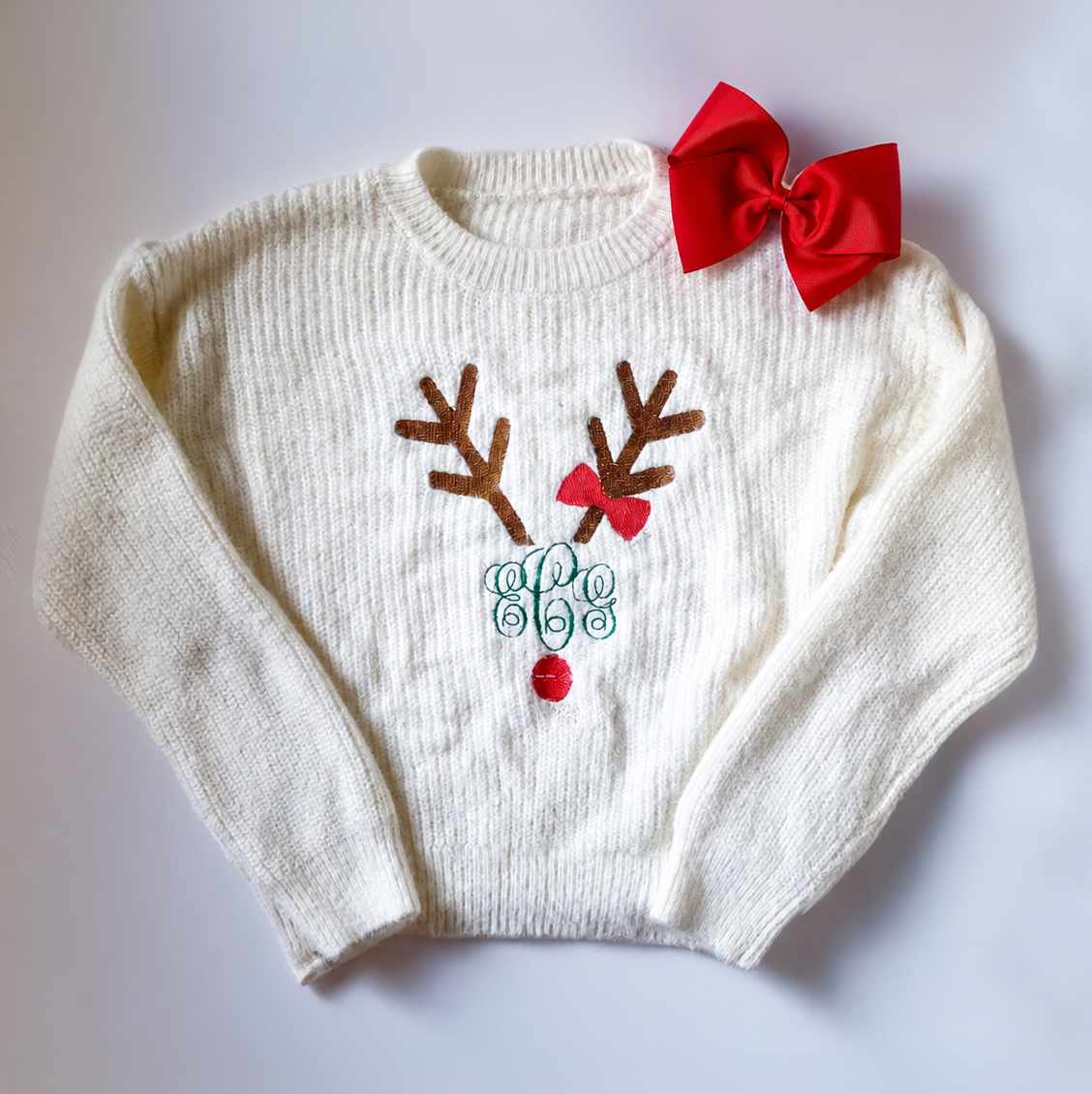 Cream children’s Christmas sweater with embroidered reindeer, red bow, and festive details.