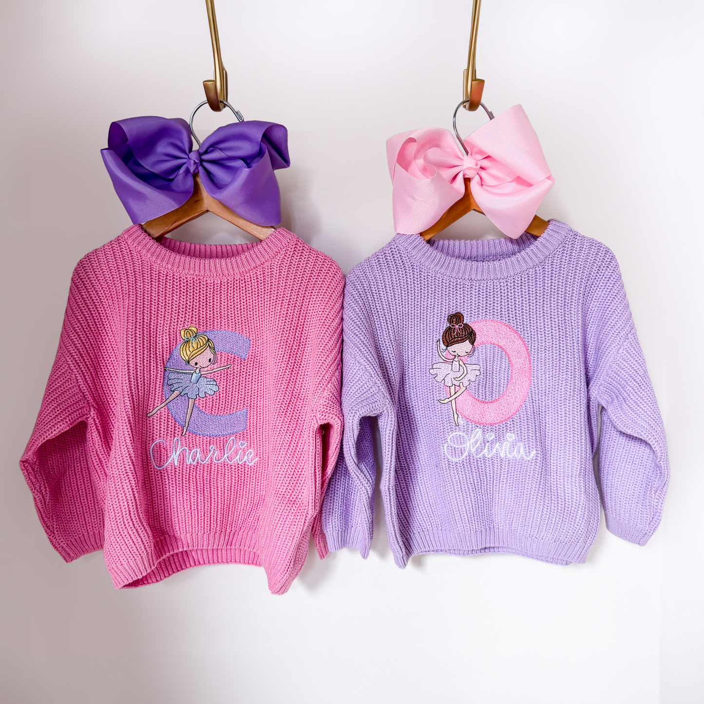 Ballet initial embroidered sweaters in pink and lavender hanging on wooden hangers with coordinating bows